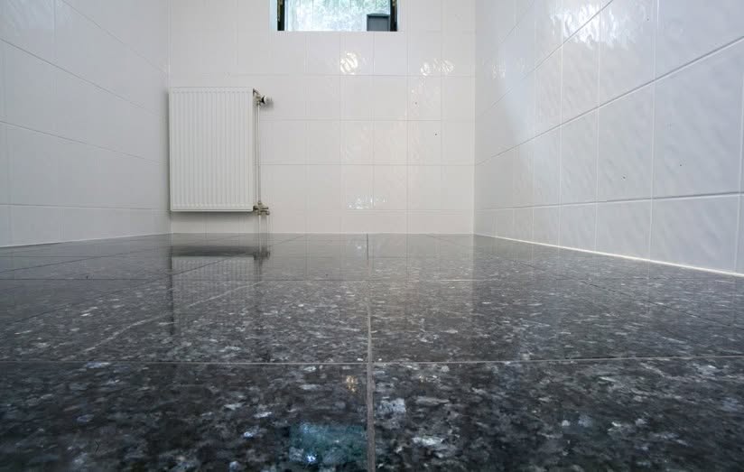 Kellerboden aus polierten Natursteinfliesen Blue Pearl, dahinter weiße Wände und Heizkörper